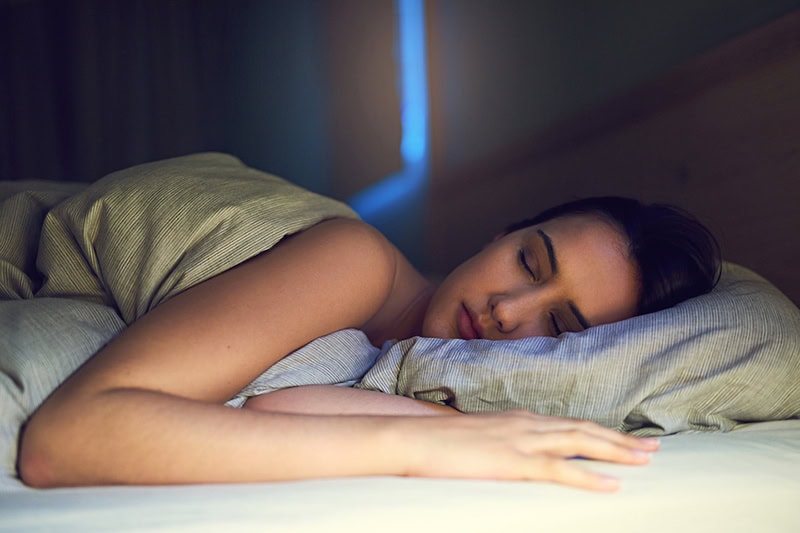 3 Health Benefits of Using Your AC While Sleeping. Shot of a young woman sound asleep in her bedroom.
